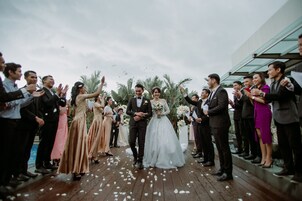 Une cérémonie de mariage où les invités se tiennent debout sur une terrasse en bois, face au couple qui avance dans l’allée.
