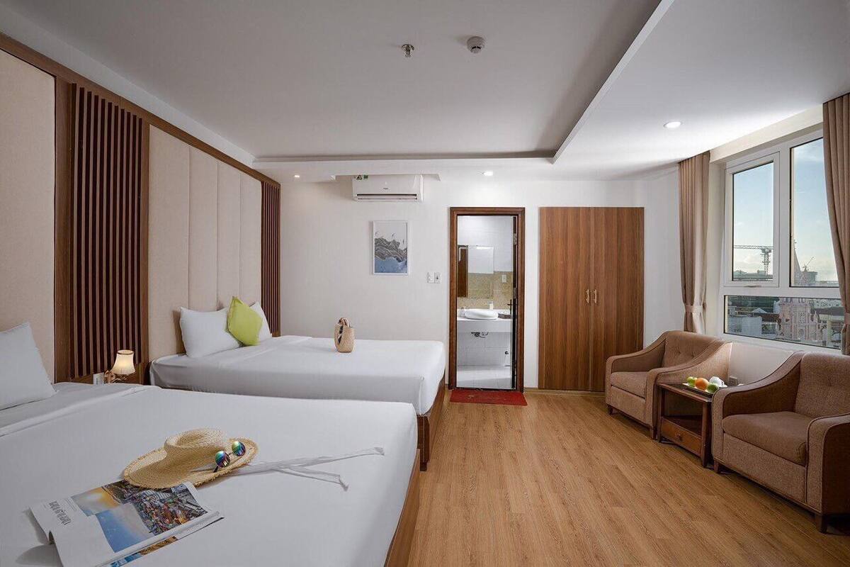 A hotel room with two beds, a sofa, a small table, and a view of the city.