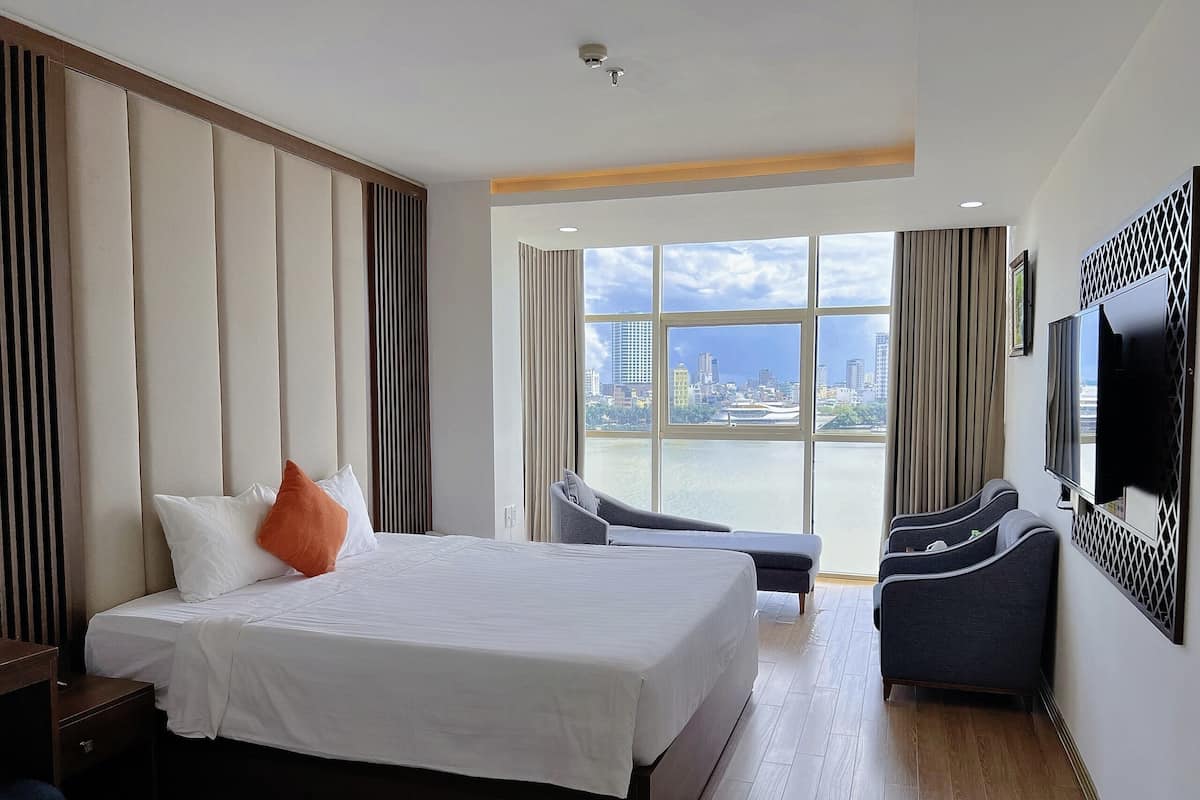 A hotel room with a large bed, a TV mounted on the wall, a seating area with a view of the cityscape.