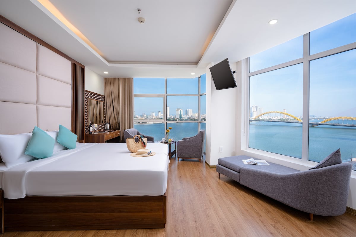 A modern hotel room with a large bed, a sofa, a TV, and a view of the city and water.