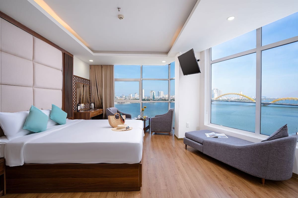 A modern hotel room with a large bed, a seating area, and a city view.