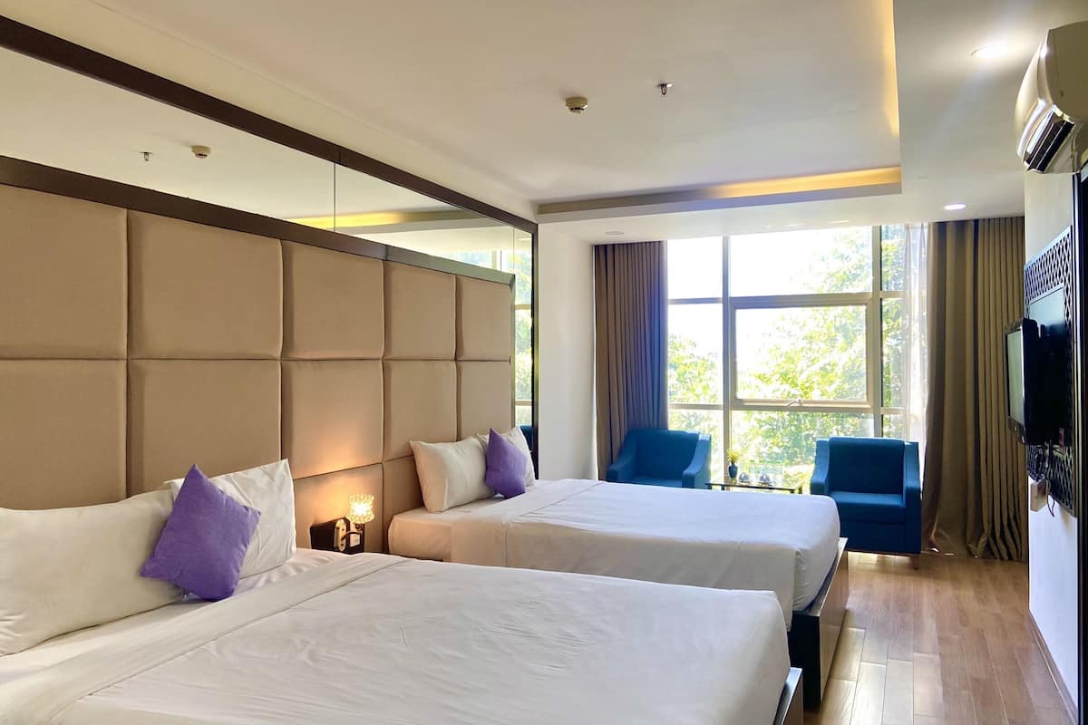 A hotel room with two beds, a large window with curtains, a television, and a ceiling-mounted air conditioning unit.