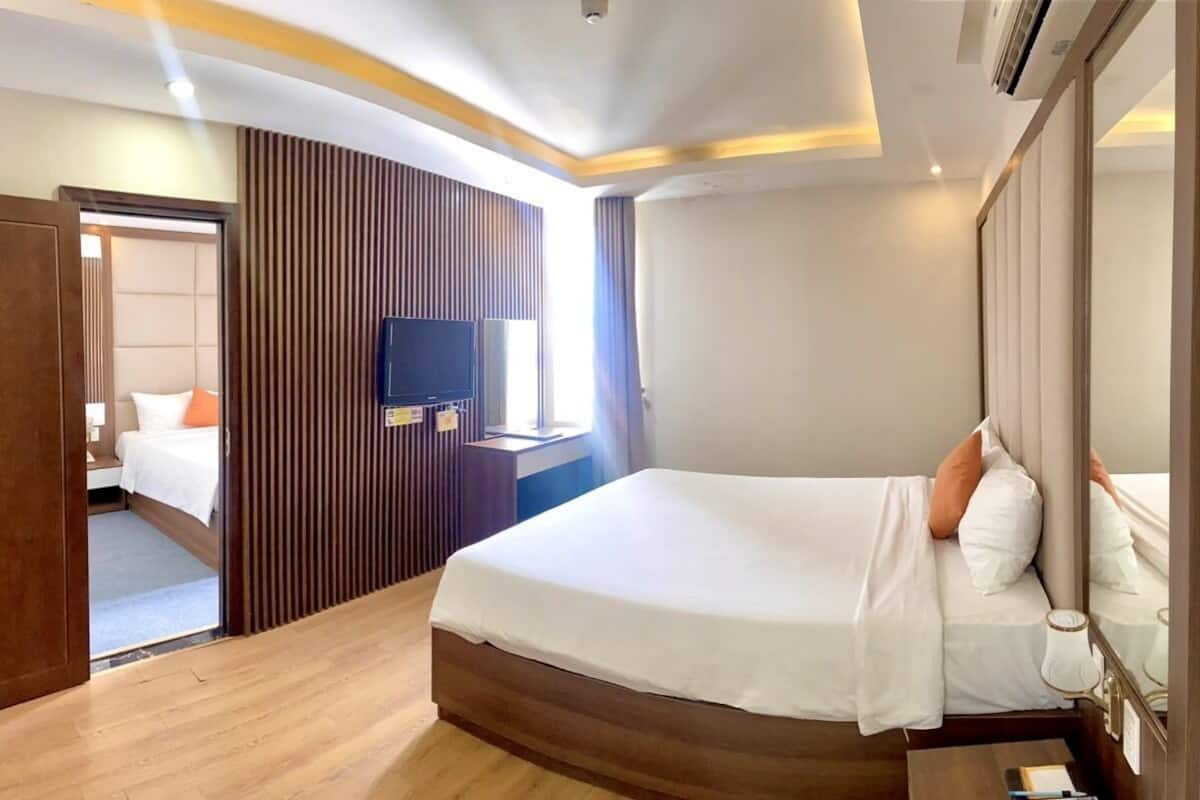 A modern hotel room with a large bed, a TV, a bedside table, and a wooden panel wall.
