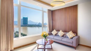 A modern living room with a large window, a sofa, a coffee table, and a decorative light fixture. - Pariat River Front Hotel (Da Nang)