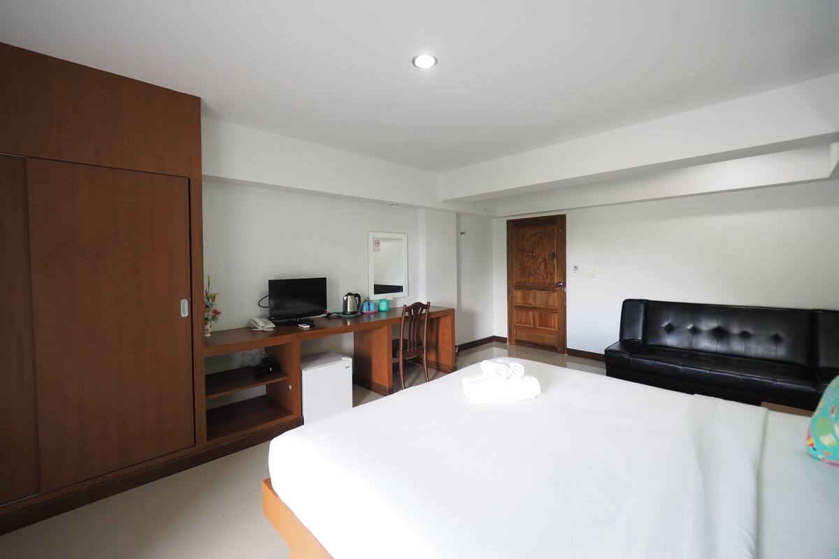 A hotel room with a bed, a desk with a computer, a television, and a wardrobe.