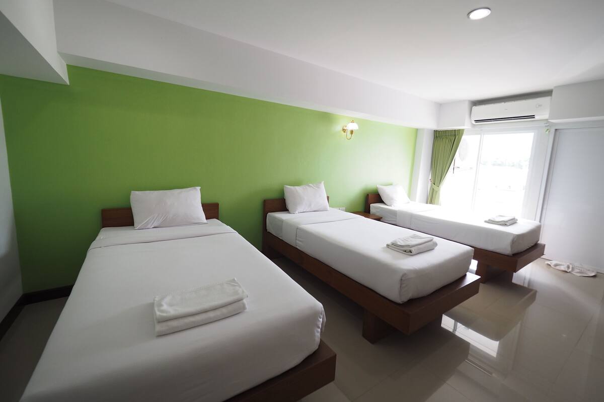 A hotel room with two beds, a green wall, and a window with curtains.