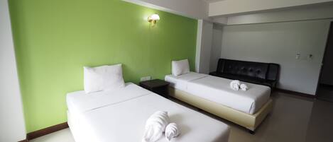 A hotel room with two beds, green walls, white bedding, a nightstand, and a wall-mounted light fixture.