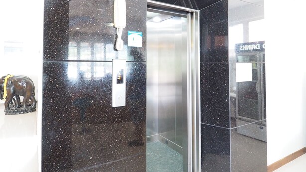 En moderne elevator med metalfinish, glasdør og kontrolpanel.