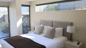 A modern bedroom with a large bed, two bedside lamps, and a view through a window. - Lakeshore Springs Apartments (Wanaka)