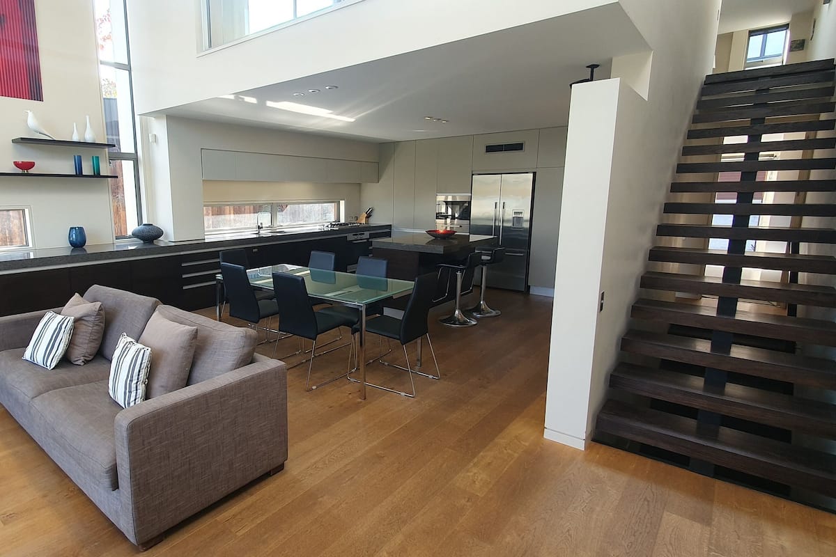 A modern living room with a sofa, a dining table, and a kitchen area in the background.