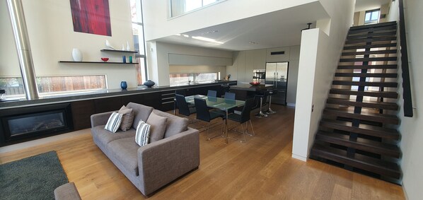 A modern living room with a sofa, a dining table, and a kitchen area in the background. - Lakeshore Springs Apartments (Wanaka)
