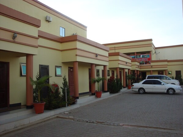 Un hotel de varios pisos, con entrada principal y zona de estacionamiento con coches.
