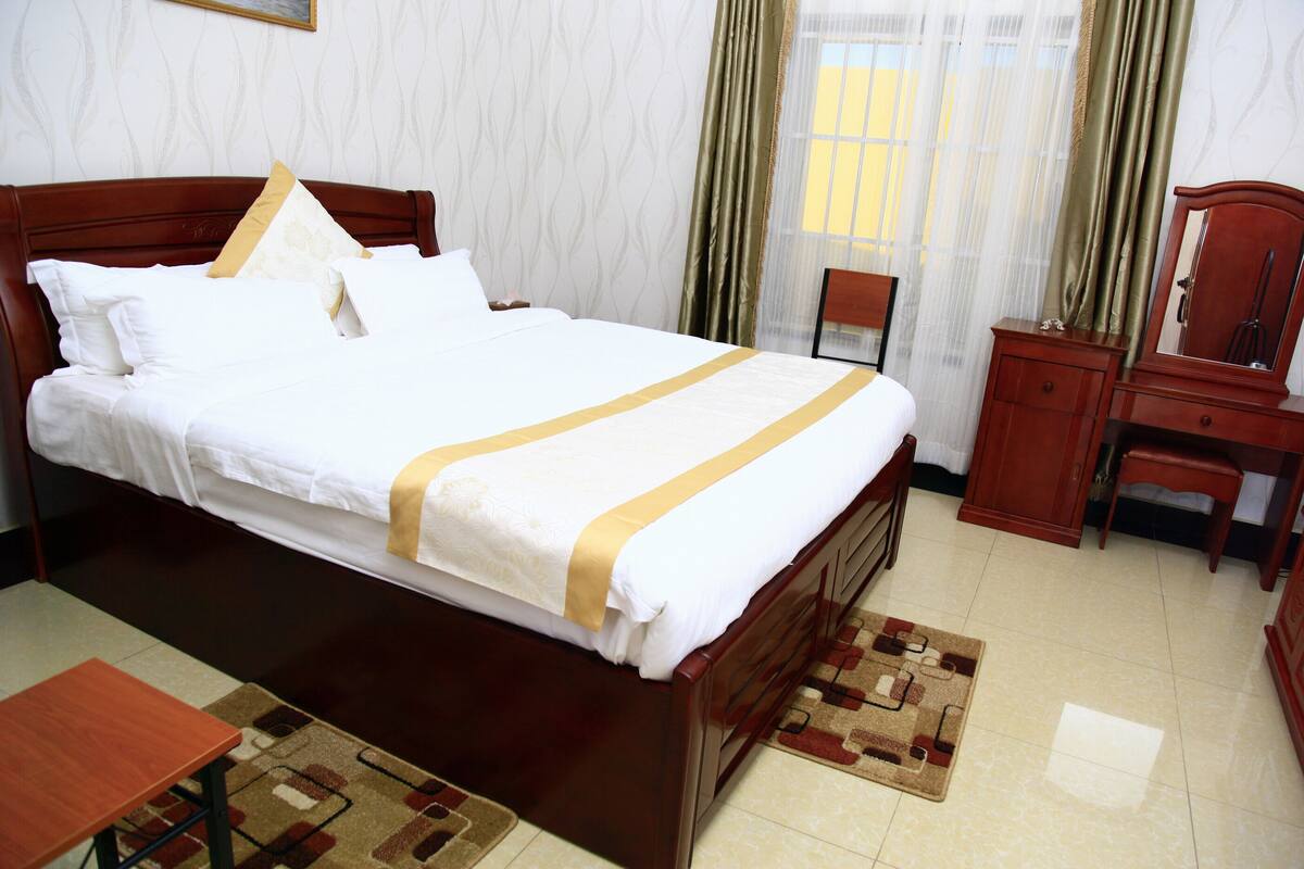 A neatly made bed with a white and gold bedspread, a wooden headboard, and a bedside table with a mirror.