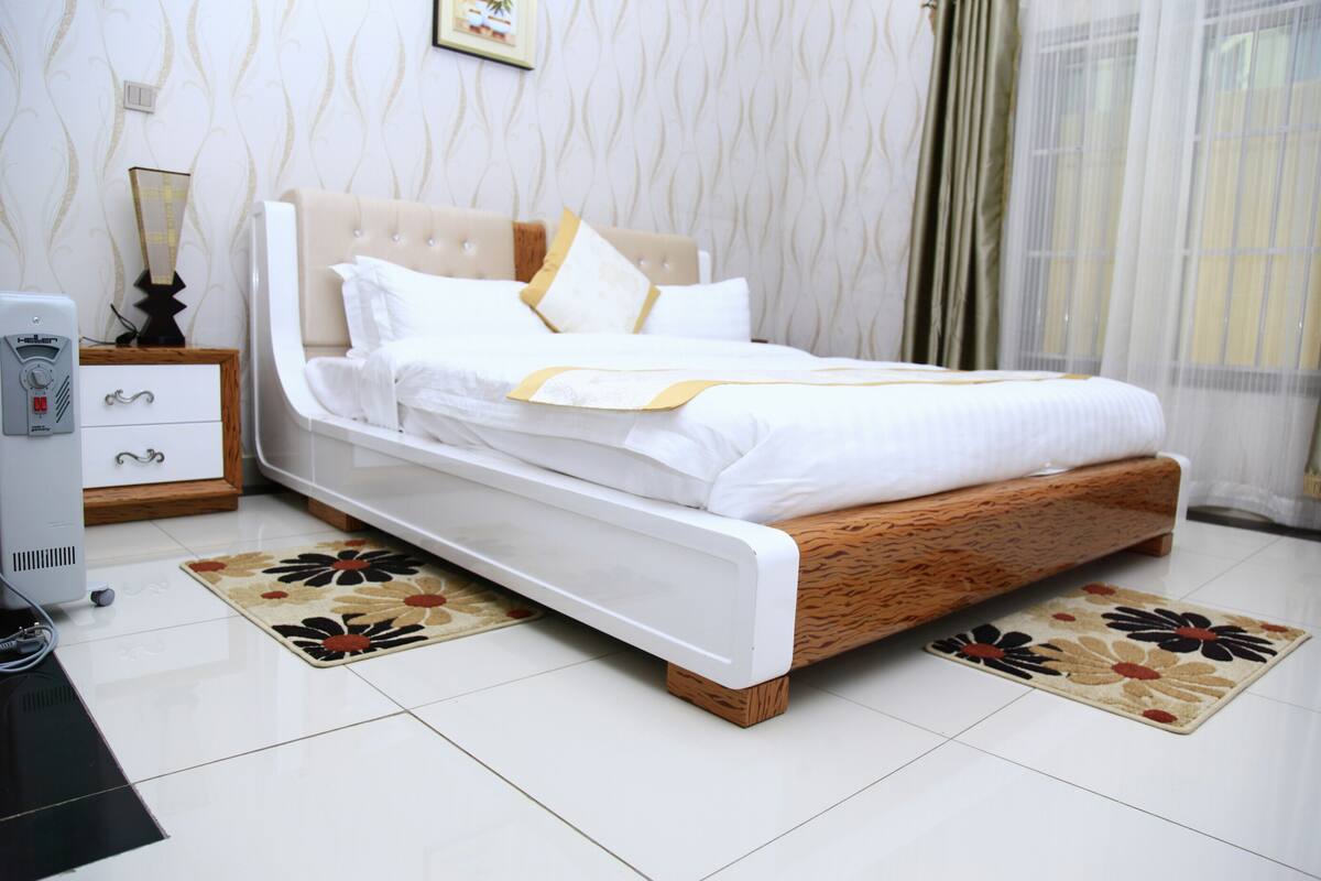 A neatly made bed with a wooden headboard, white bedding, and a floral-patterned rug.