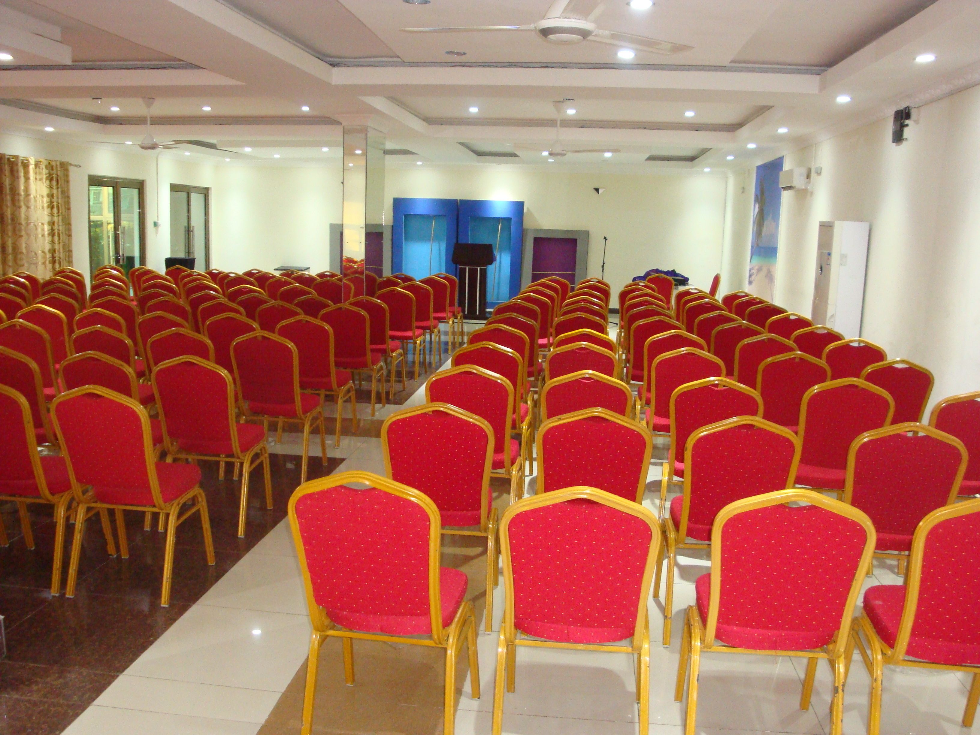 A conference room with rows of red chairs and a stage at the front.