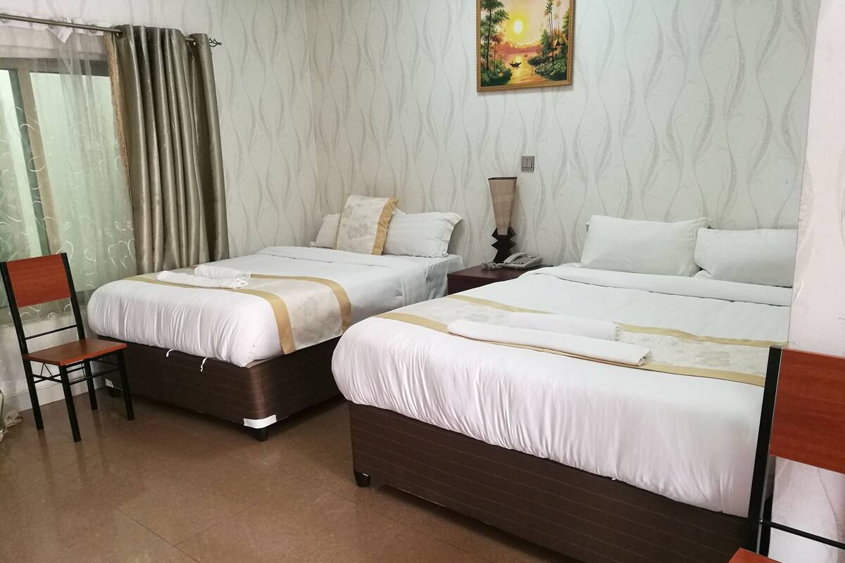 A hotel room with two beds, a chair, a nightstand, and a painting on the wall.