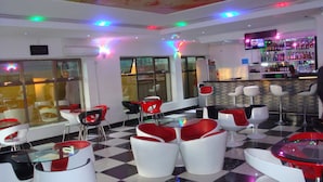 A bar area with a checkered floor, red and white chairs, and a bar counter with bottles. - Golden Zambezi Lodge (Lusaka)