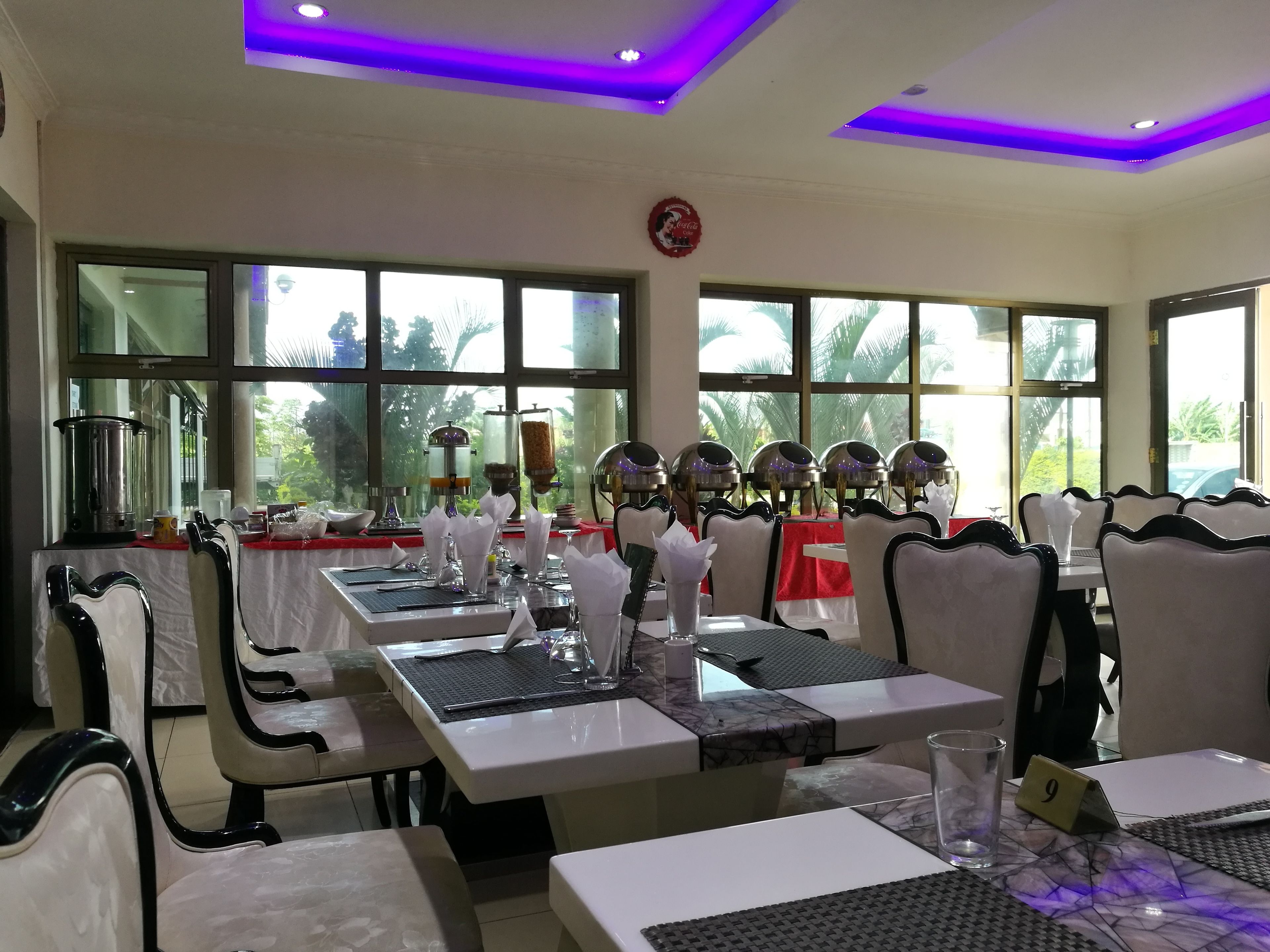 A restaurant with tables set for dining, a view of the outdoors, and a ceiling with purple lighting.