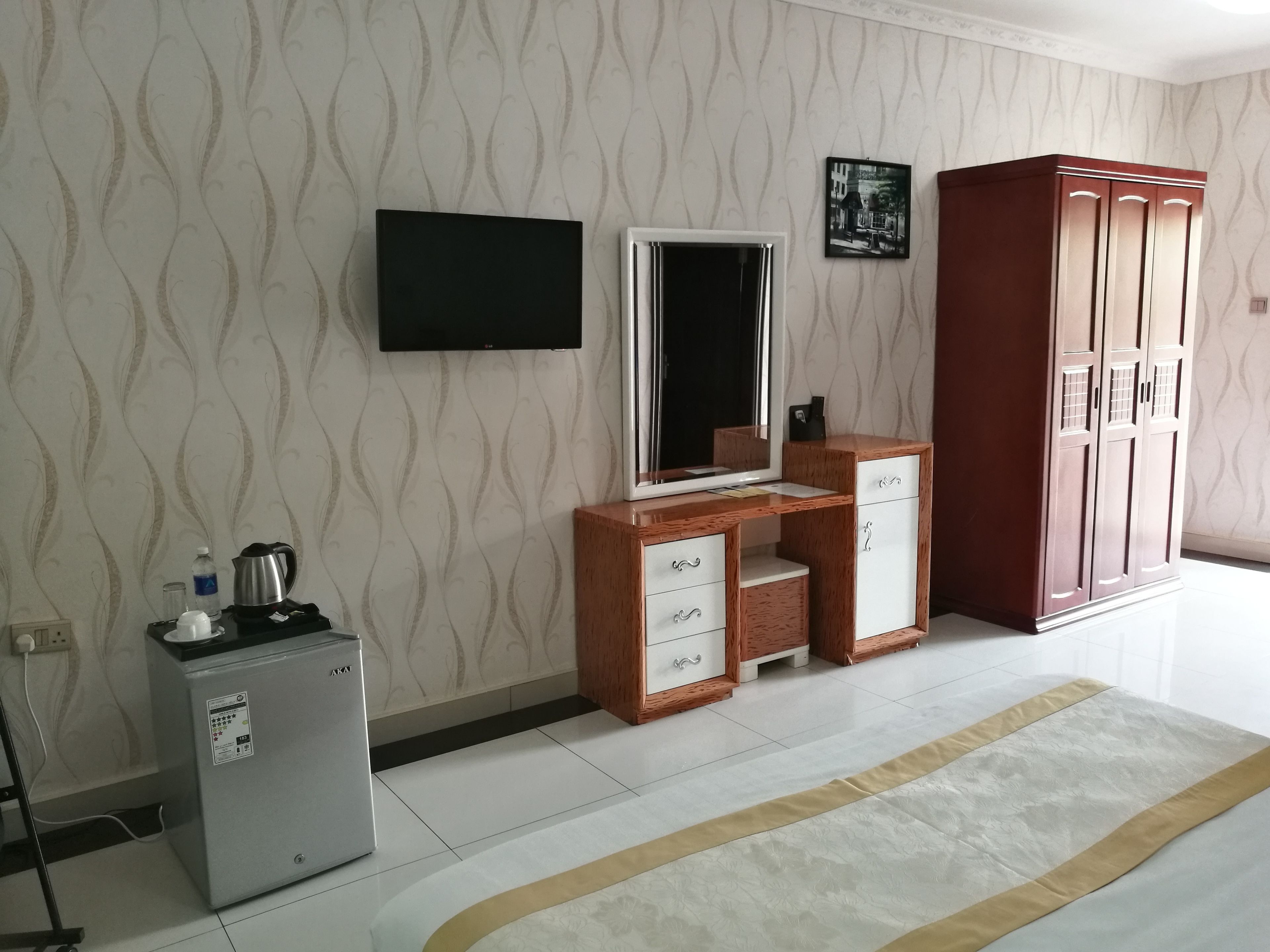 Une pièce comprenant un bureau en bois, un téléviseur fixé au mur, une armoire et un petit réfrigérateur.