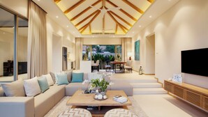A modern living room with a sofa, coffee table, ottomans, and a TV. - Trichada Villas by RESAVA (Choeng Thale)