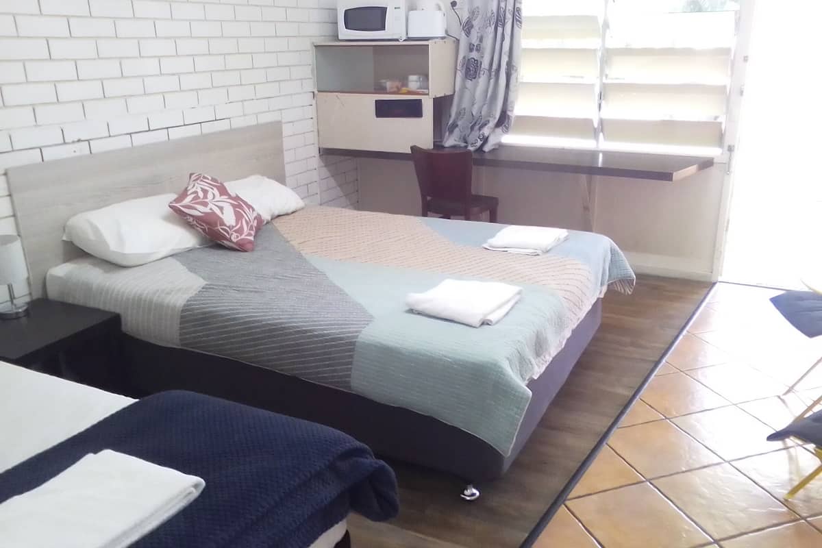 Quarto de hotel com cama, mesa de cabeceira, micro-ondas e uma pequena mesa.