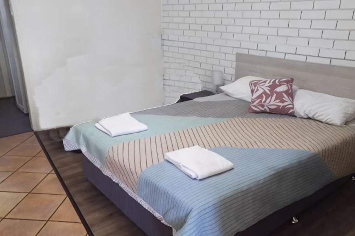 A bed with striped bedding, a pillow with a leaf pattern, and a blanket folded on top.