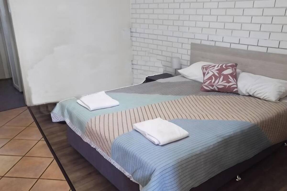 A bed with striped bedding, a pillow with a leaf pattern, and a blanket folded on top.