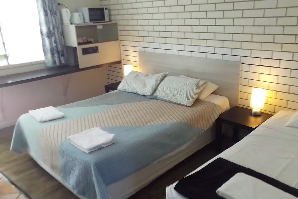Uma cama bem arrumada com colcha listrada e almofadas, uma mesa de cabeceira com abajur e uma parede de tijolos brancos.