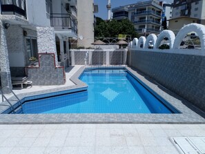 Piscina com deck ladrilhado, parede de pedra e cerca de metal.