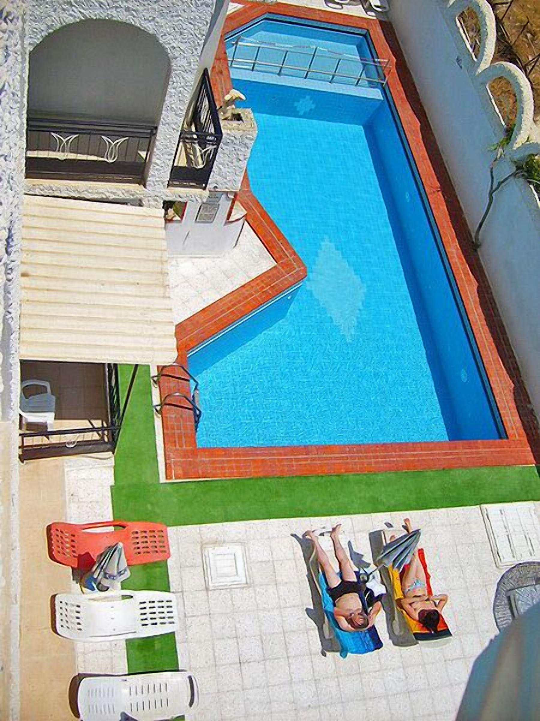 An aerial view of a swimming pool with a tiled deck, a small patio area, and a few lounge chairs.