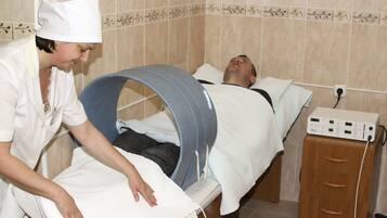 A healthcare professional attends to a patient in a treatment room with a bed and a cabinet.