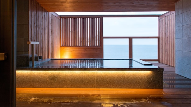 Un moderno espacio de spa con techo de madera, una bañera de hidromasaje con vidrio y vista al mar.