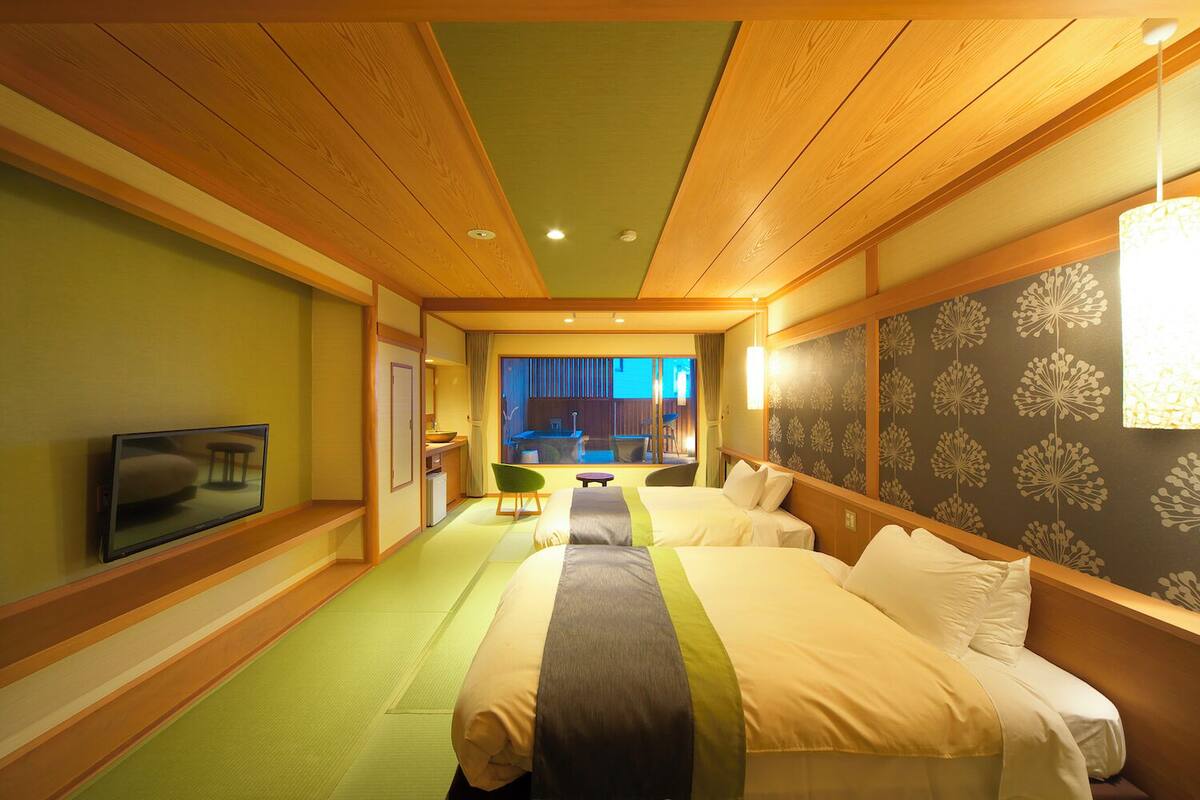 Een hotelkamer met twee bedden, een televisie, een klein tafeltje en uitzicht op buiten.