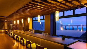 Un área de bar moderna con una barra larga, varias sillas e iluminación colgante.
