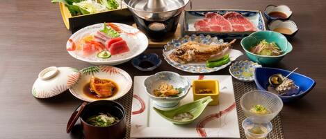 A variety of Japanese dishes including sashimi, tempura, and a hot pot, arranged on a table with traditional utensils.