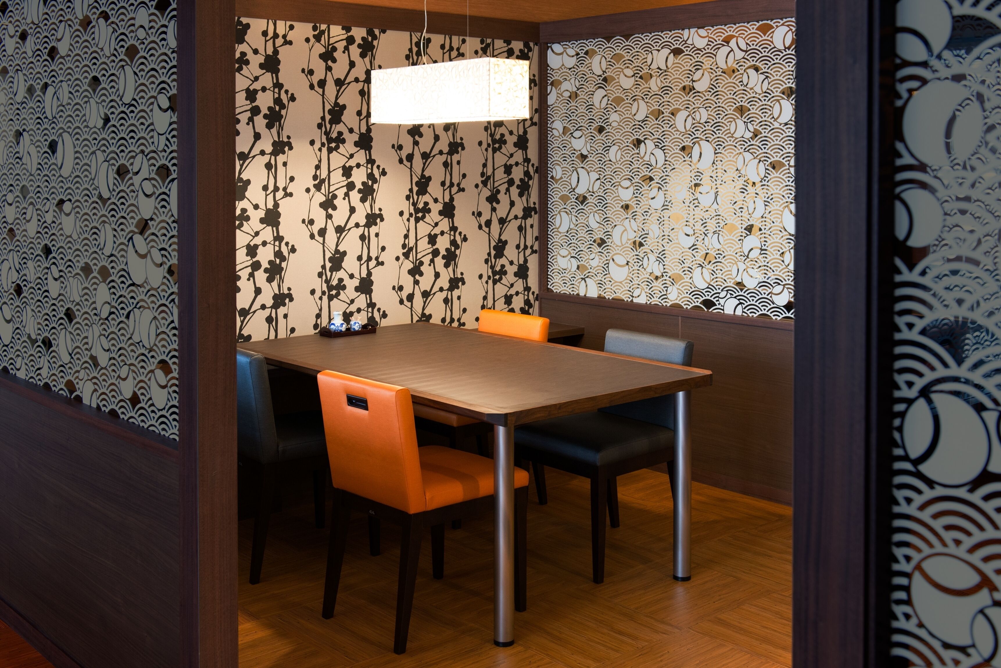 Zona pranzo con tavolo e sedie in legno, lampadario a sospensione e pannelli decorativi a parete.