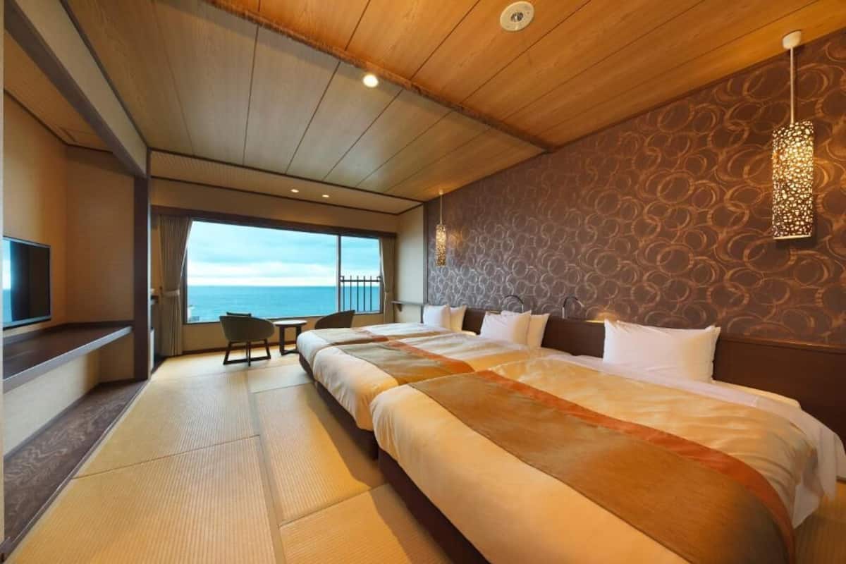Een hotelkamer met een groot bed, een televisie, uitzicht op zee en een behang met een patroon.
