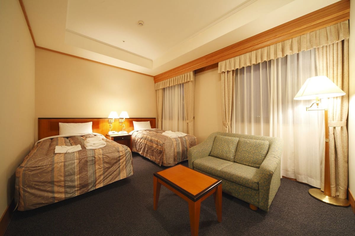 A hotel room with two beds, a sofa, a small table, and a lamp.