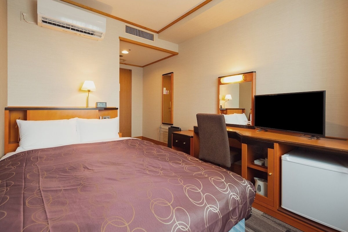 A hotel room with a bed, desk, TV, and a small refrigerator.