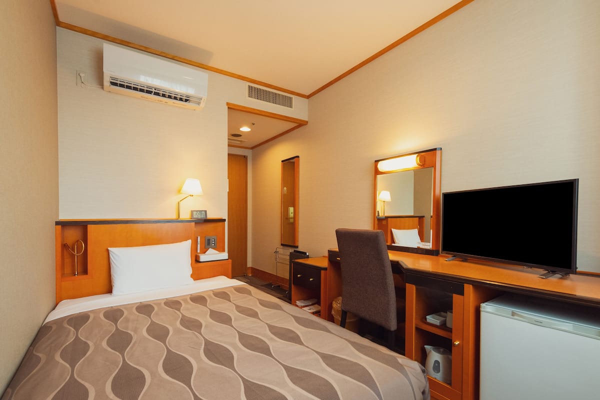 A hotel room with a bed, desk, chair, television, and a refrigerator.