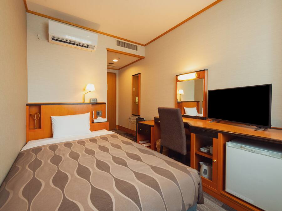 A hotel room with a bed, desk, chair, television, and a refrigerator.
