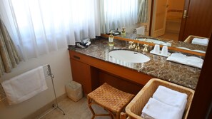 Un baño con lavamanos de mármol, un espejo, un taburete de mimbre y una pequeña cesta de mimbre con toallas.