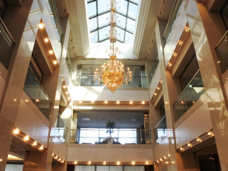 Ein mehrstöckiges Atrium mit einer imposanten Chandelier, Glasgeländern und Tageslicht durch Oberlichter.