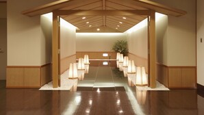 A reception area with a wooden ceiling, a central aisle, and rows of chairs with lamps. - Hotel Racine Sinmaebashi (Maebashi)
