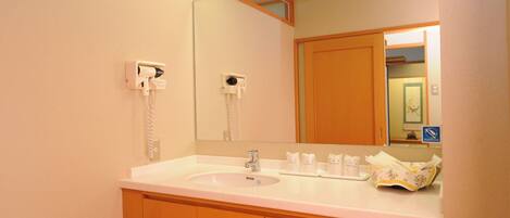 A hotel bathroom with a white sink, wooden cabinets, a mirror, and a telephone.