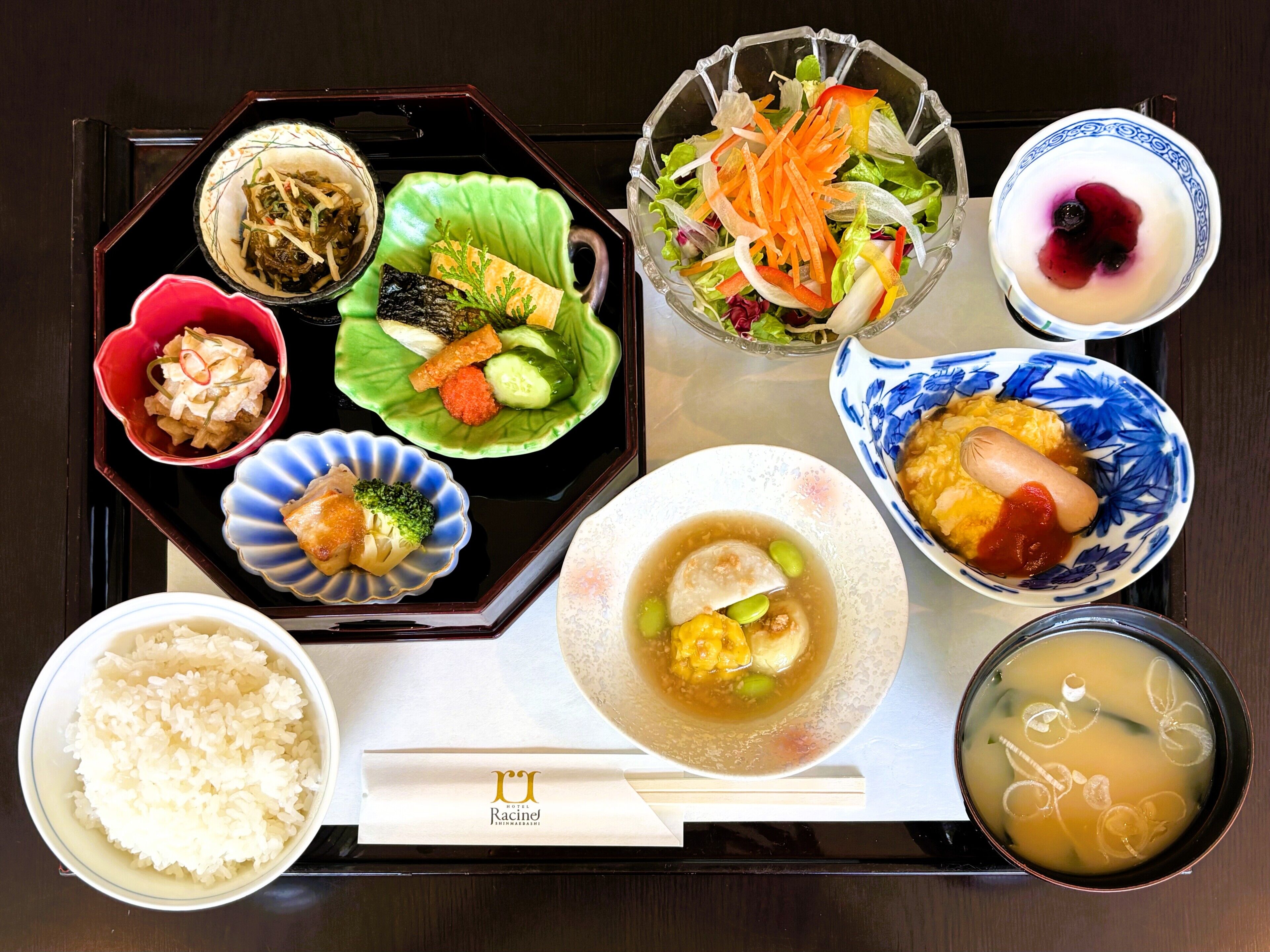 Variedad de platos japoneses dispuestos en una bandeja, incluyendo arroz, sopa y diferentes tipos de sashimi y ensalada.