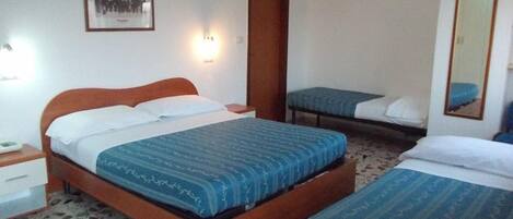 A hotel room with a large bed, a smaller bed, a bedside table, a nightstand, a wall-mounted light, a framed picture, and a mirror.