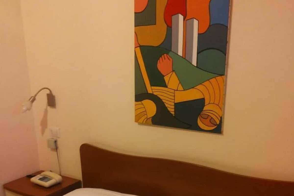 A hotel room with a bed, a nightstand with a phone, and a colorful abstract painting on the wall.