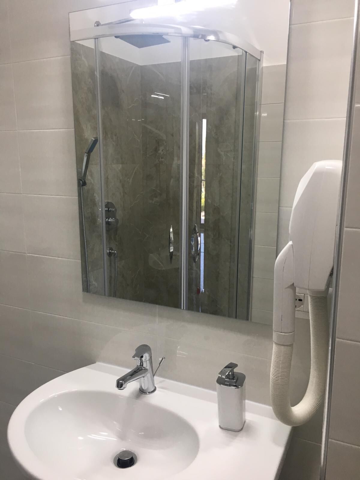 Un baño moderno con ducha envuelta en vidrio, un lavabo blanco con grifo cromado y un cabezal de ducha de mano.