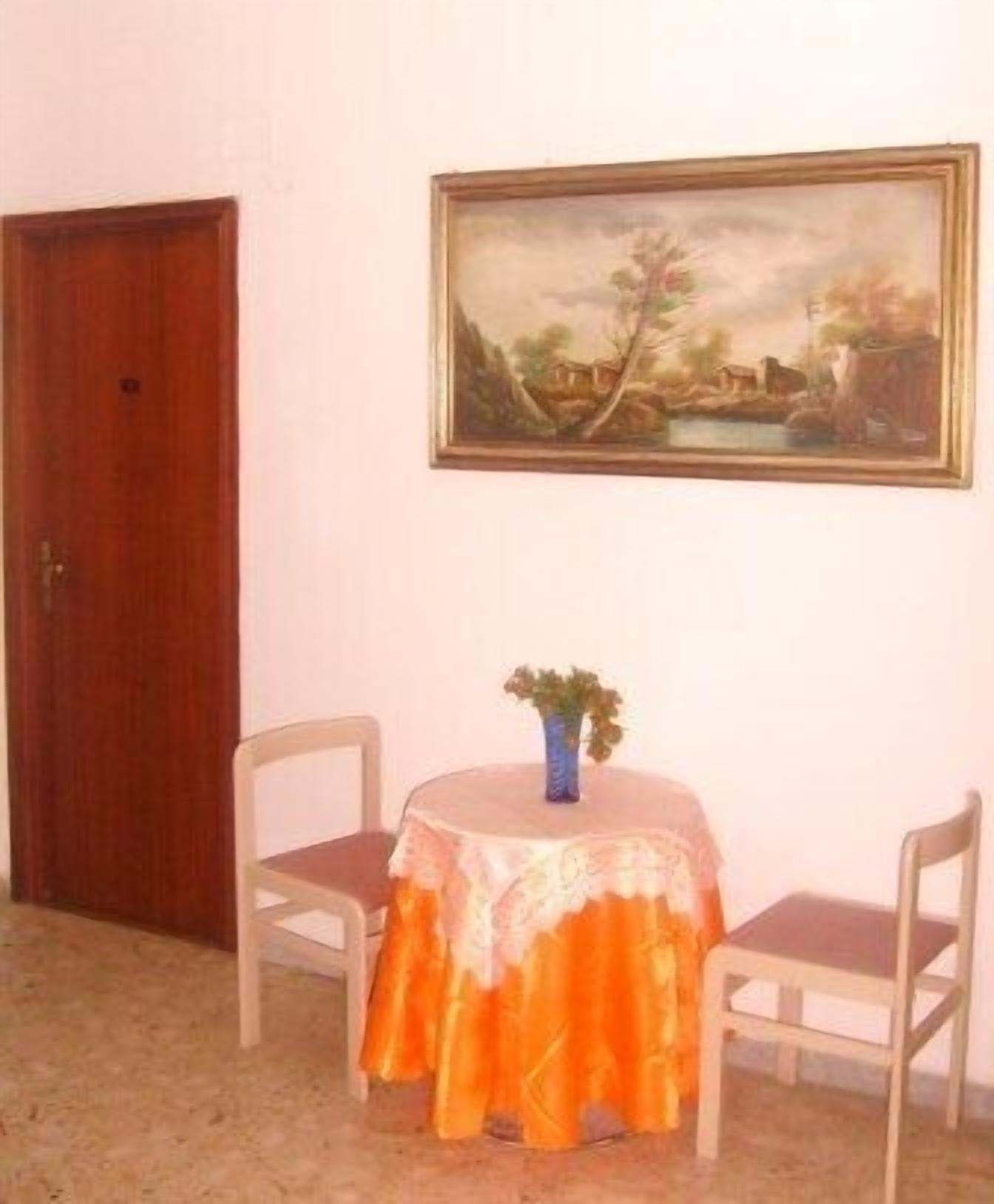 Une pièce avec une porte en bois, une table recouverte d’une nappe à motifs floraux, deux chaises et un tableau accroché au mur.